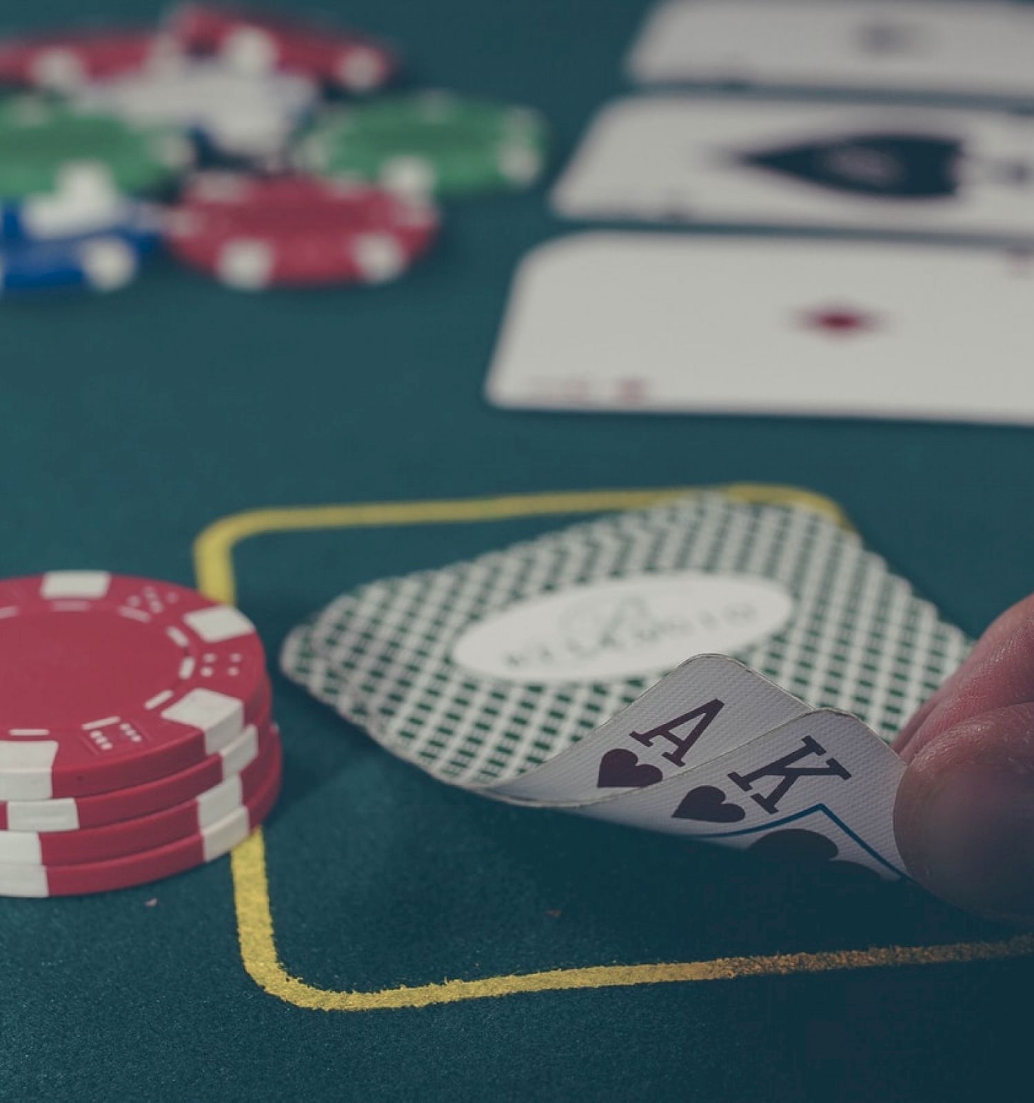 A poker game is in progress with a hand holding ace and king of hearts, and poker chips and cards visible on the table ending the sentence.