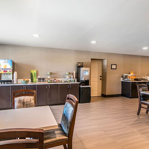 This image shows a breakfast area with tables and chairs, a counter with food and drink dispensers, and a clean, modern design ending the sentence.