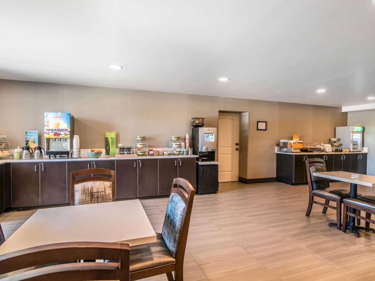 A dining area with tables, chairs, and a counter offering food and drink options, including a beverage machine and various condiments.